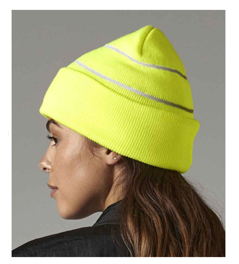 Person wearing a bright yellow beanie with reflective stripes on a gray background